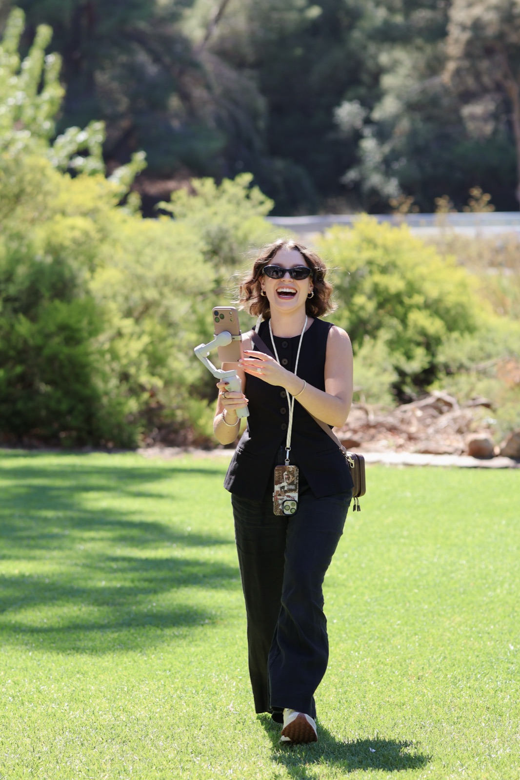 Jaeli walking across a lawn at an Adelaide wedding, laughing while filming candidly